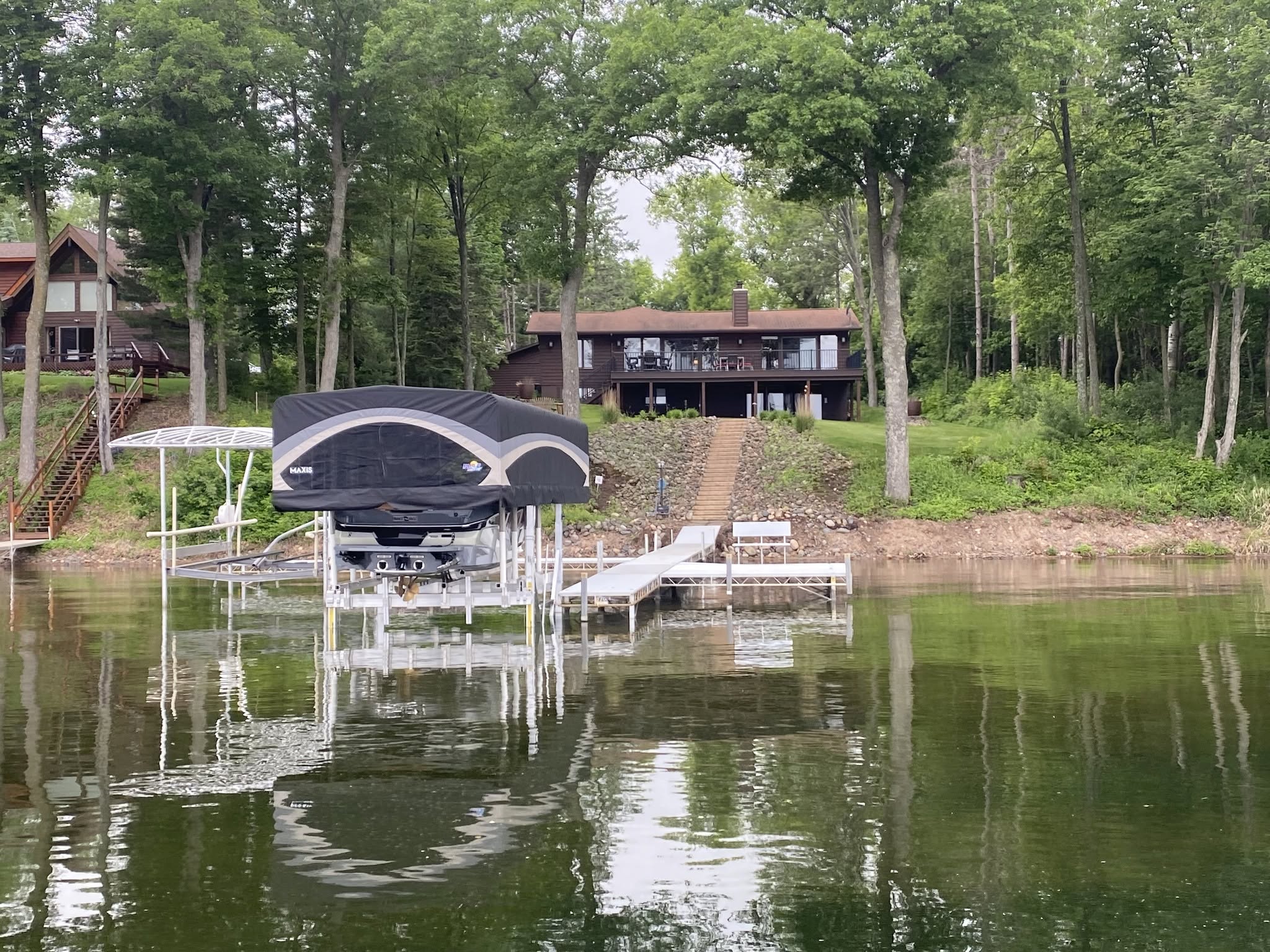 Wake boat raised on a canopied boat lift beside a wooded lakefront